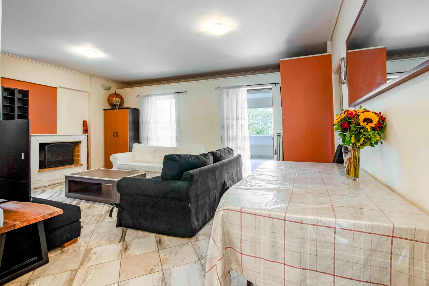 A bright living room with a black sofa, a white sofa, a fireplace, and a dining table with a bouquet of flowers.