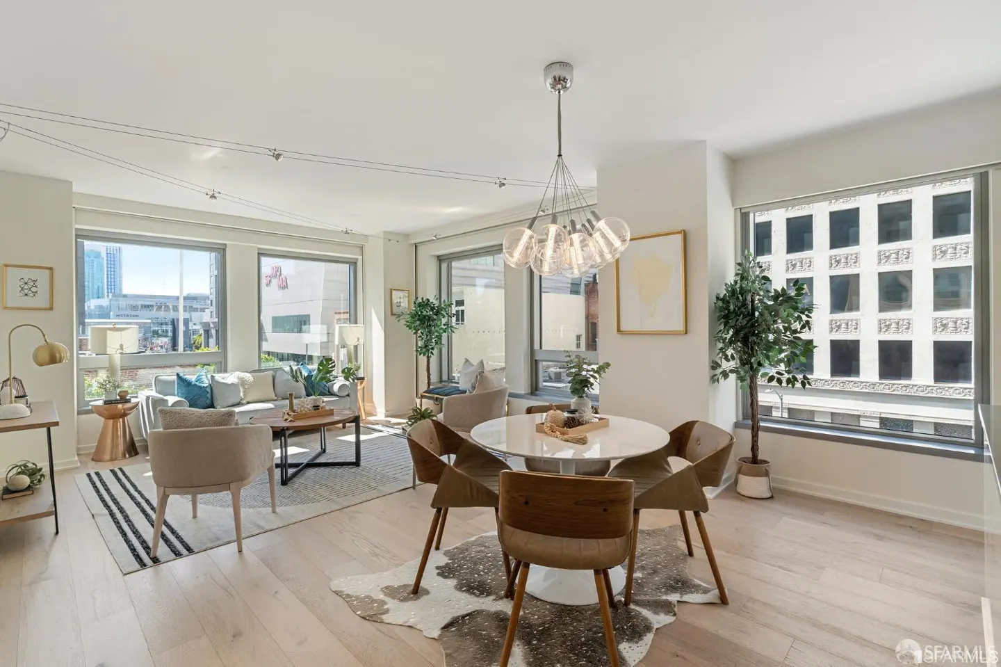 Bright, modern living space with a round white table, brown chairs, and a cowhide rug. Large windows offer city views.