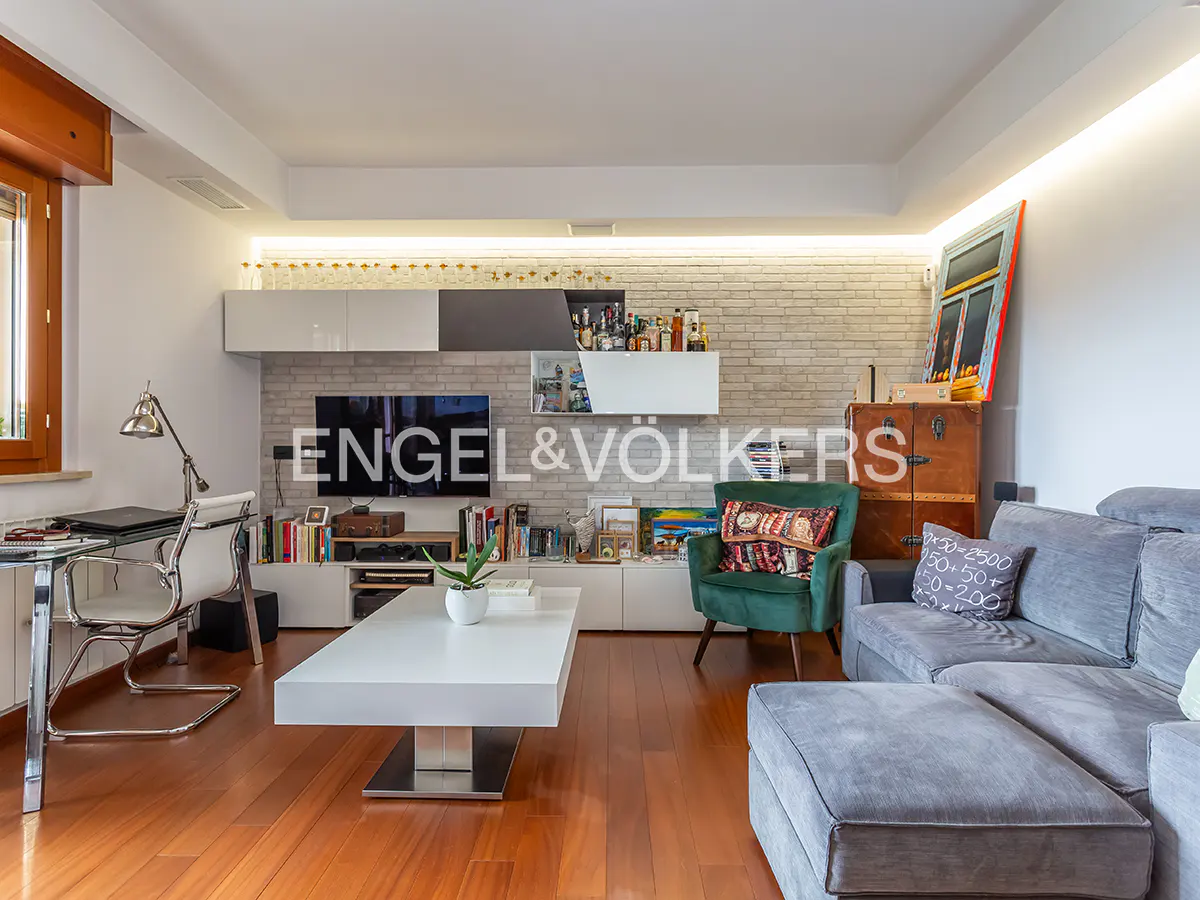 Living room with hardwood floors, gray sofa, green chair, and white coffee table. A desk and TV are against a white brick wall.