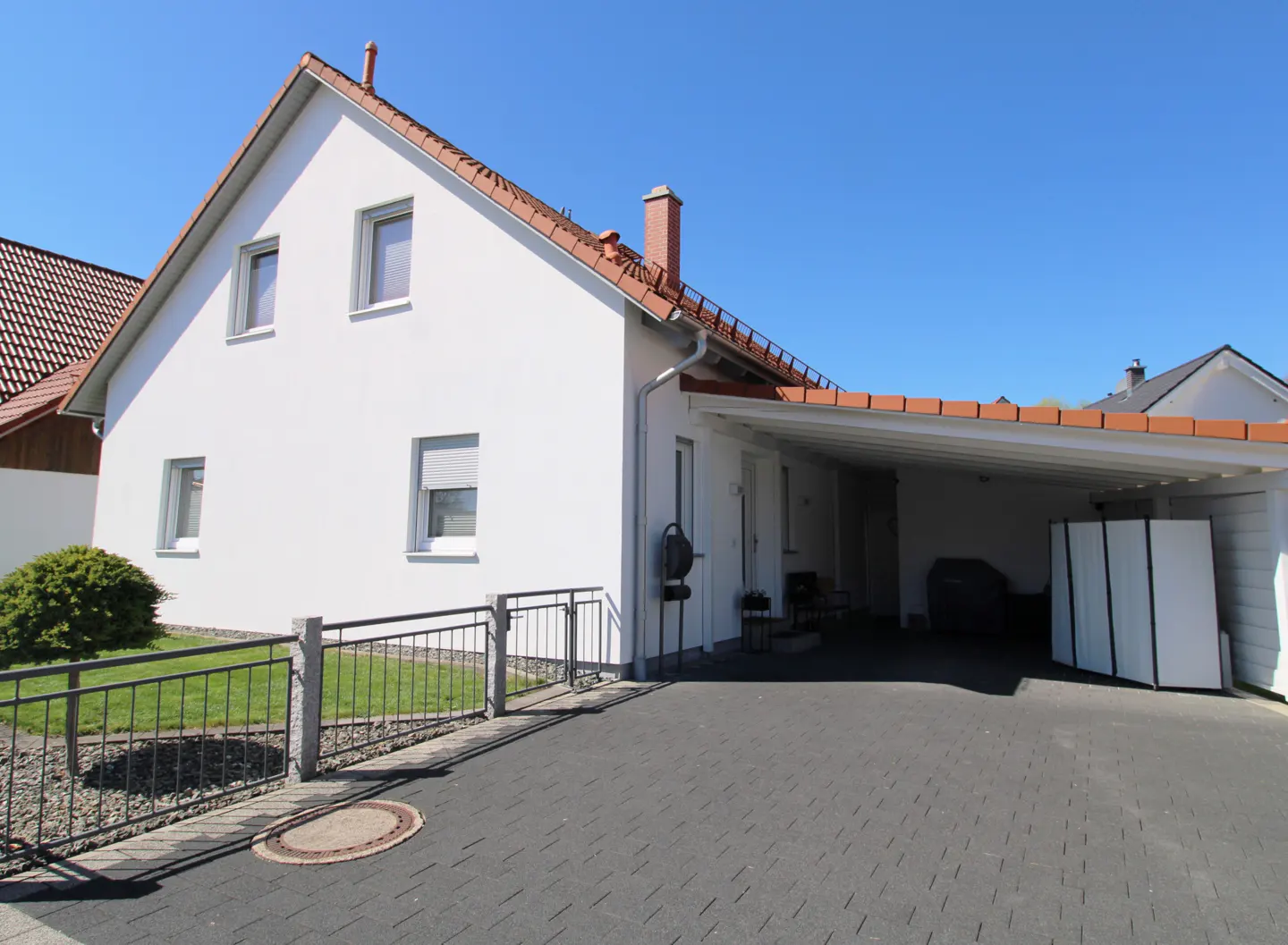 A white, two-story house with a red-tiled roof and a carport on a sunny day.