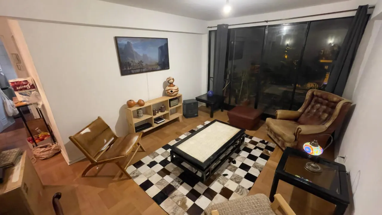 A cozy living room with a brown leather chair, a black and white rug, and a wooden coffee table. A large window shows a night view.