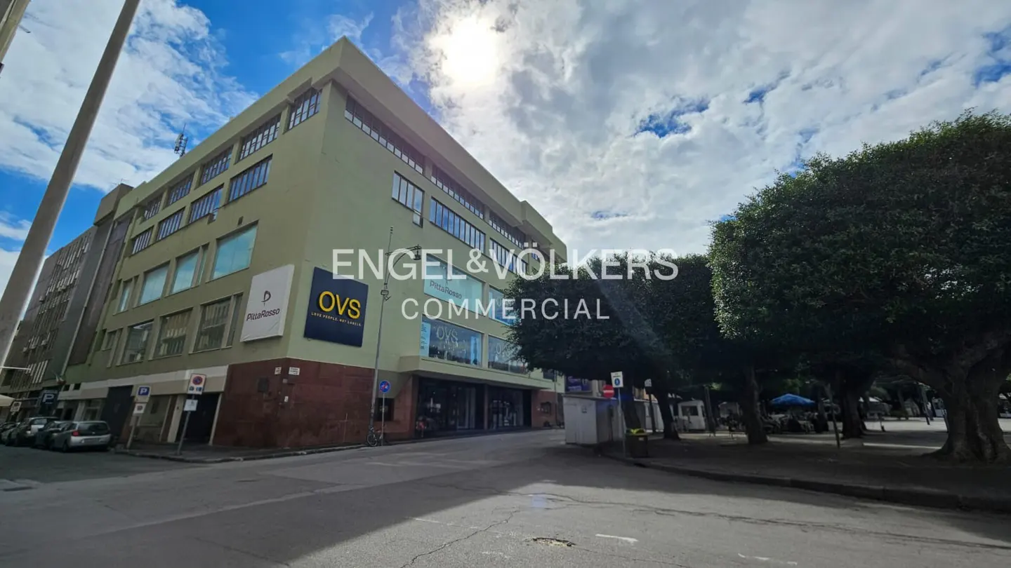 Exterior view of a multi-story commercial building with "Engel & Völkers Commercial" signage, OVS and PizzaRossa stores, and a park nearby.
