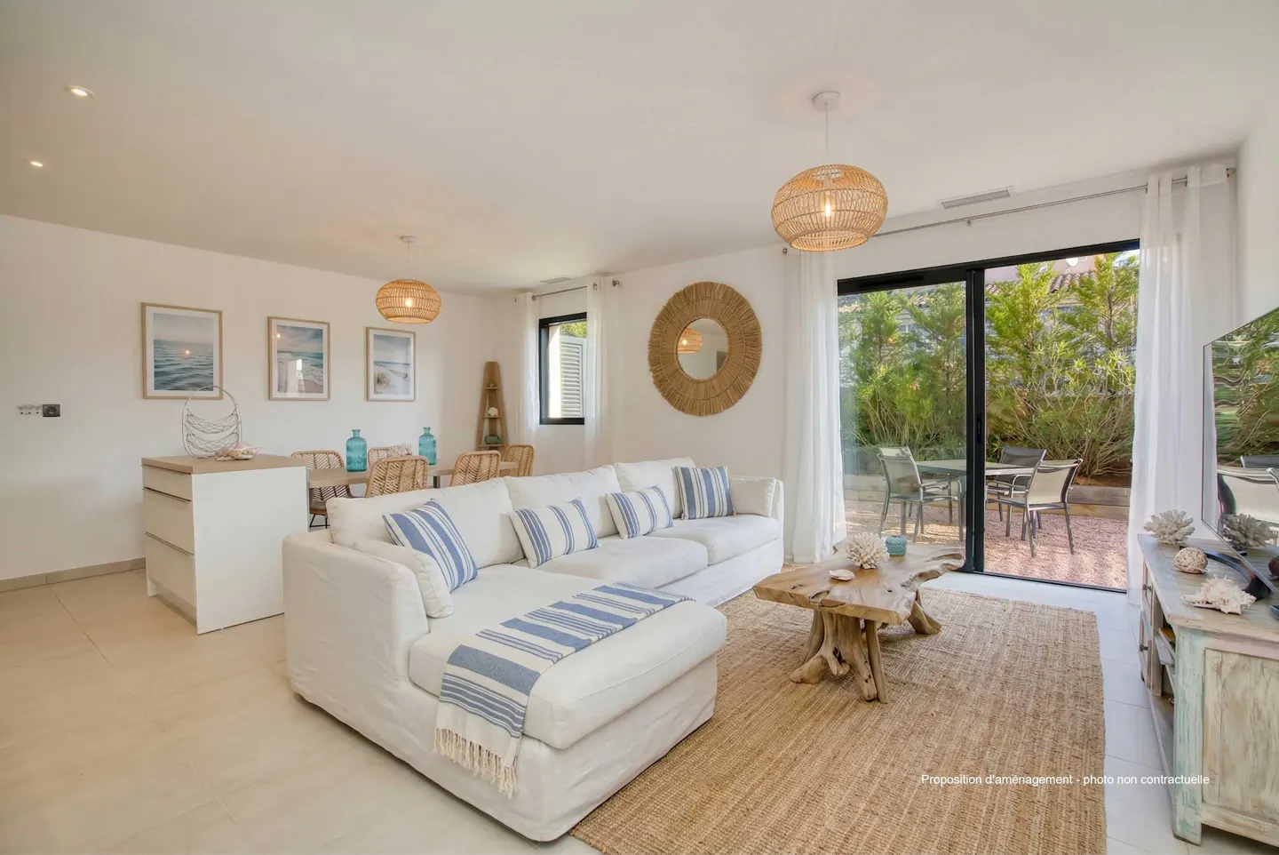 Bright living room with white sofa, wood table, and jute rug. Patio visible through sliding glass doors. Coastal decor.