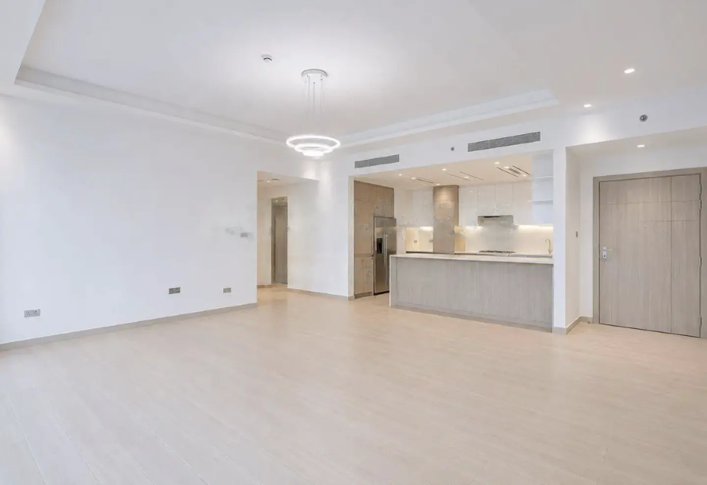 Modern open-plan living area with light wood floors, white walls, a contemporary chandelier, and a sleek kitchen island.