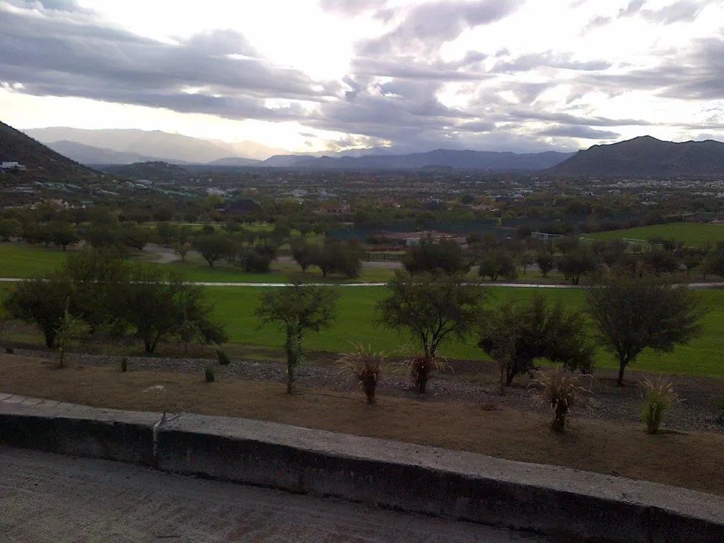 Scenic view of a green valley with trees, mountains, and a cloudy sky.