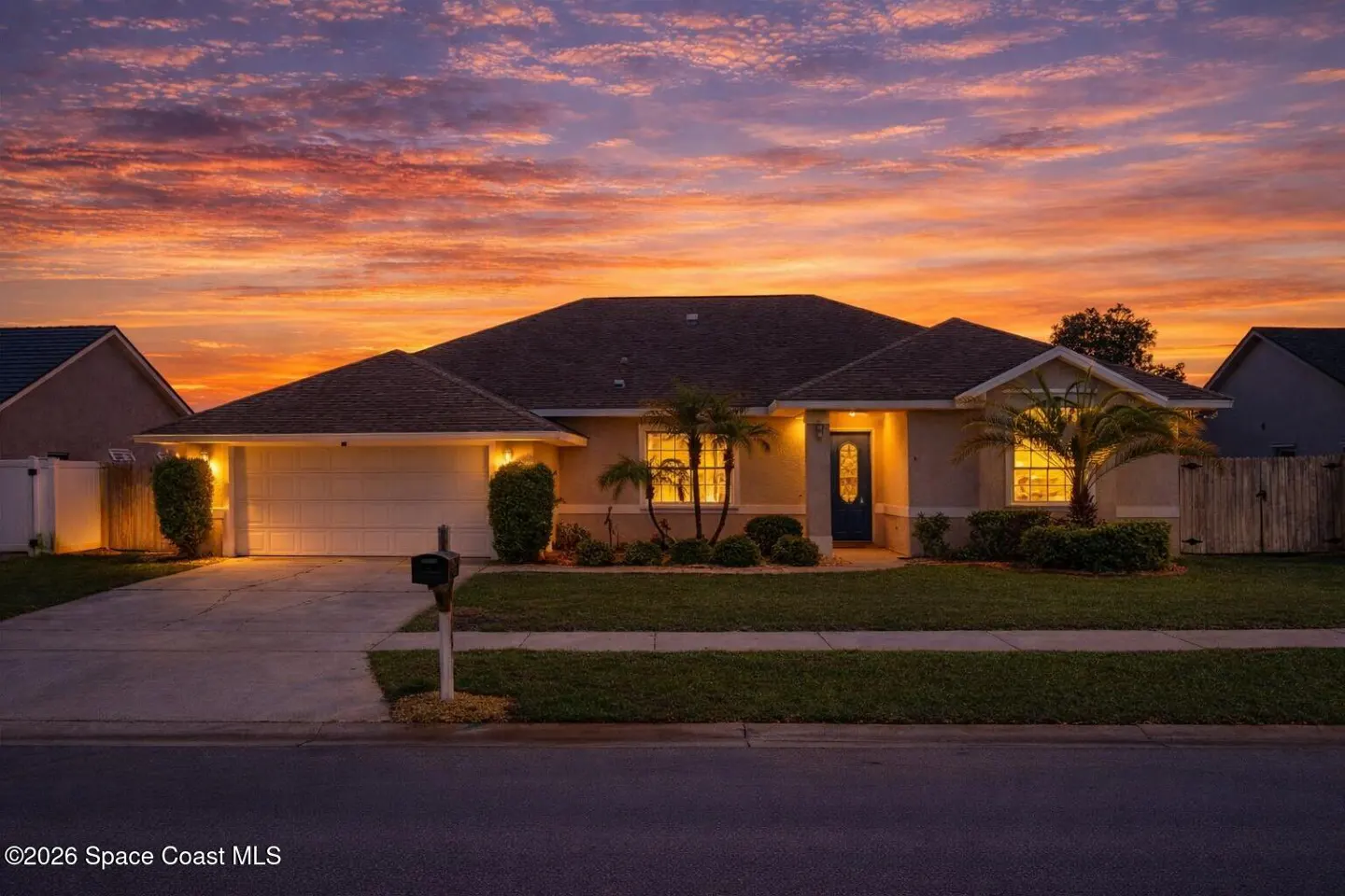 Tan single-story house with a brown roof, blue door, and palm trees at sunset.