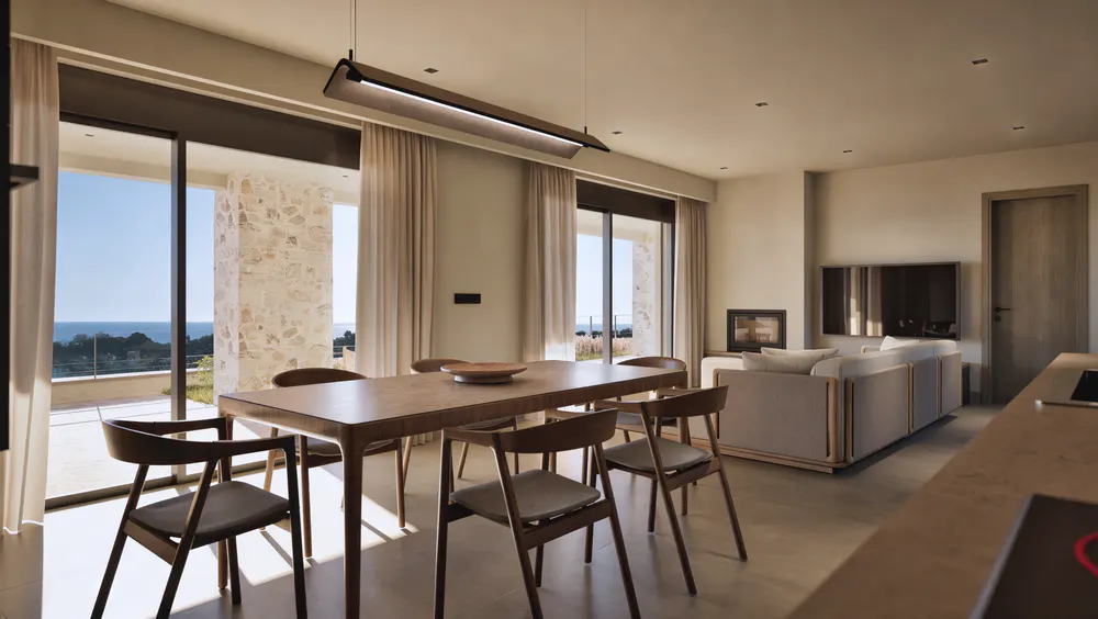Modern dining area with wooden table and chairs, overlooking a sea view through large glass doors, with a living room nearby.
