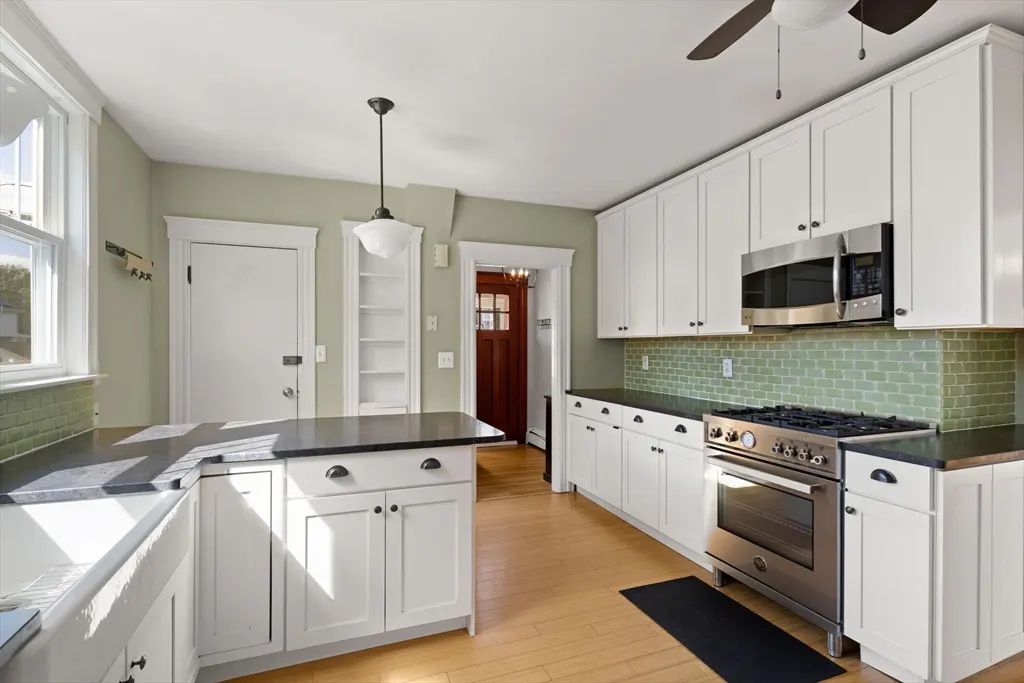 A bright kitchen with white cabinets, black countertops, and light green walls. A stainless steel oven and microwave are visible.