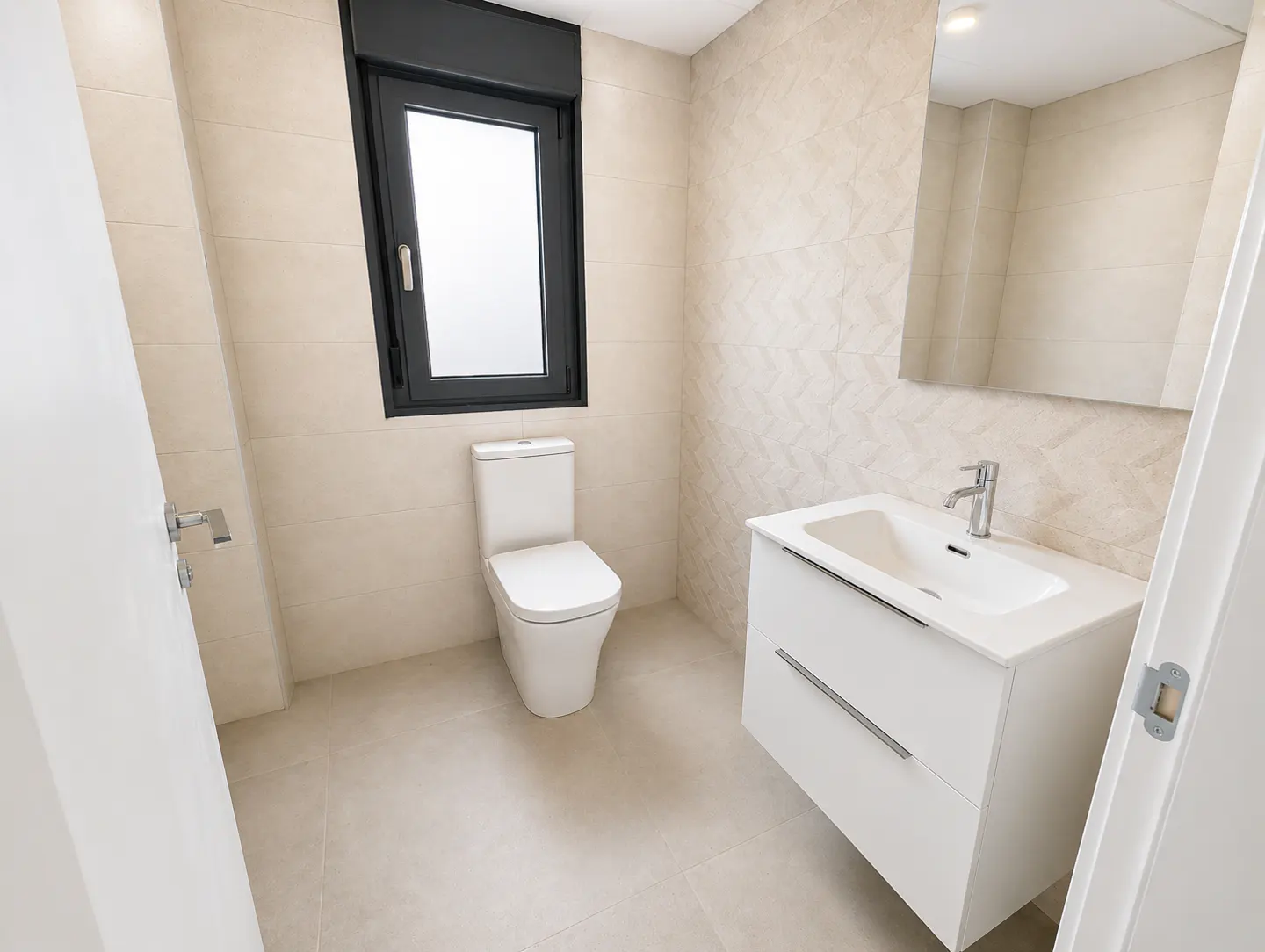 Bright bathroom with beige tile, white toilet and vanity, and a black-framed window.