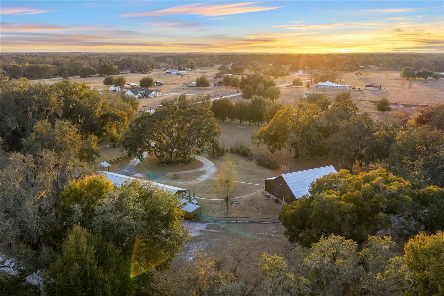 Aerial view of a rural property at sunset, featuring a barn, trees, and open fields.