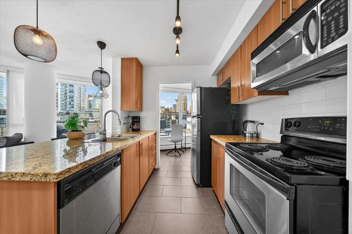 A modern kitchen with wood cabinets, granite countertops, and stainless steel appliances. A city view is visible through a doorway.