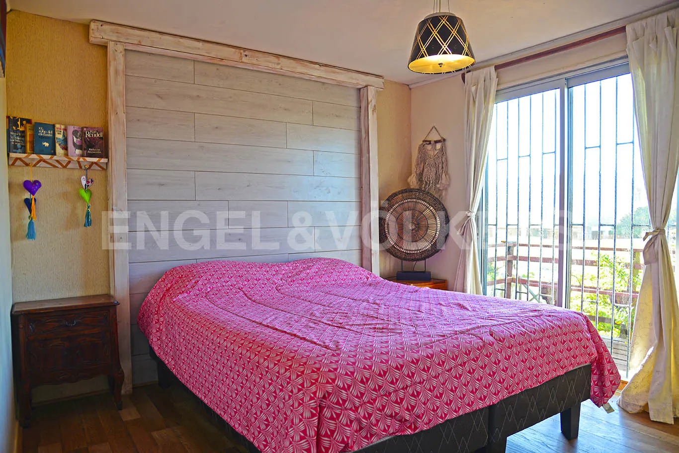 Bedroom with a pink patterned bedspread, a wooden headboard, and a sliding glass door to a balcony.