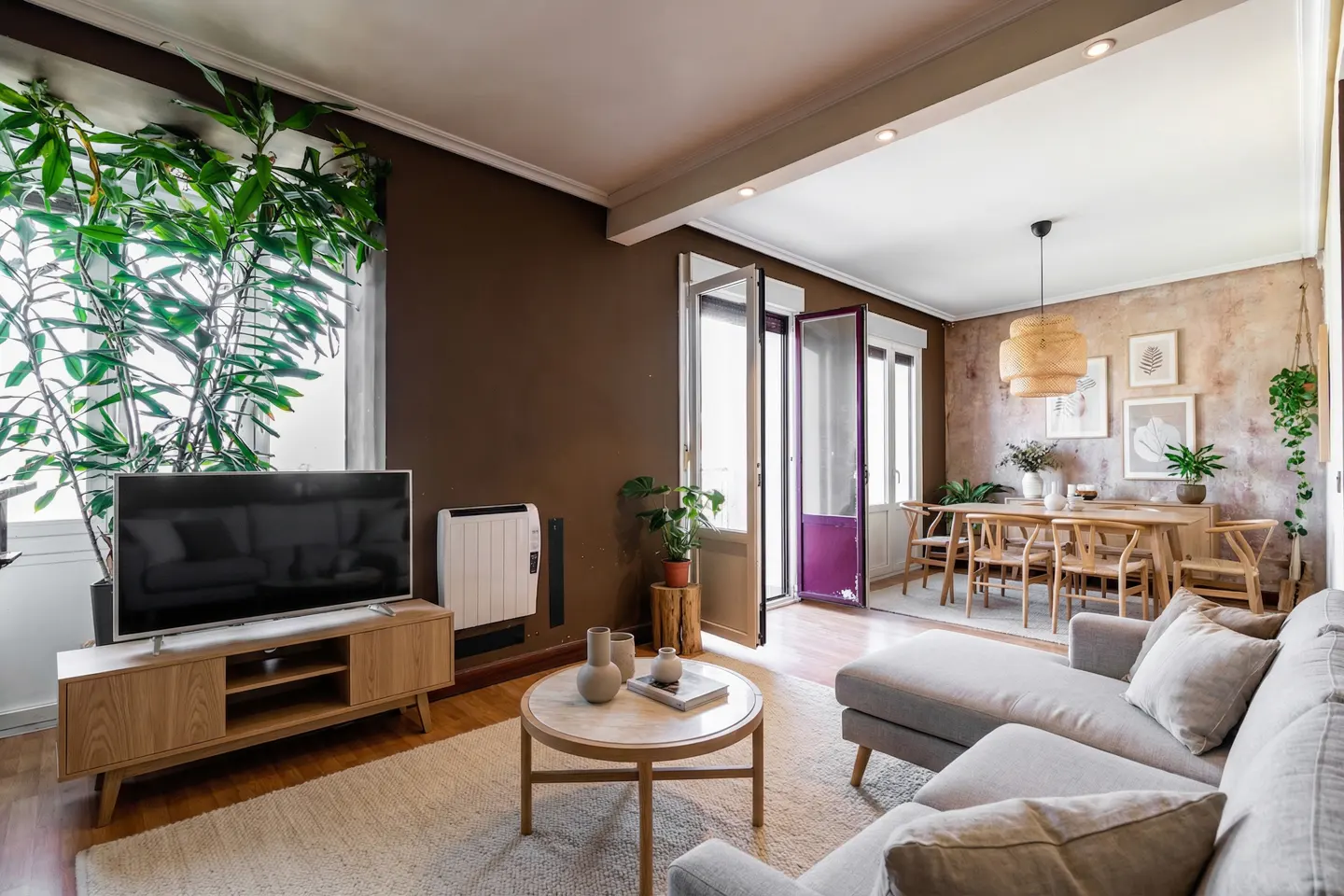 Living room with a gray sofa, wood table, and TV. A dining room is visible through an open doorway.