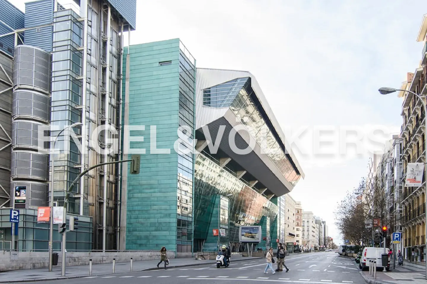 Street view of modern buildings with glass and green facade, people crossing the street, and cars on the road.