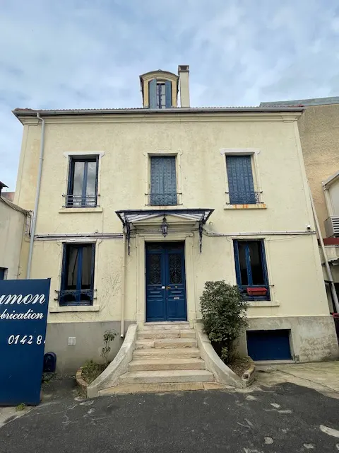 Two-story beige building with blue window shutters and a blue double-door entrance with stone steps.