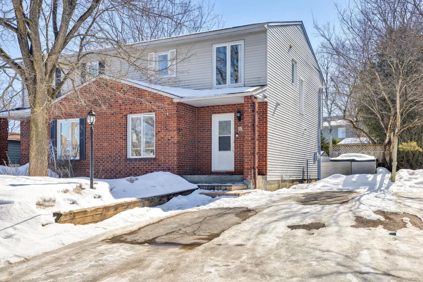 Two-story house with red brick and gray siding, white door, and snow-covered yard.