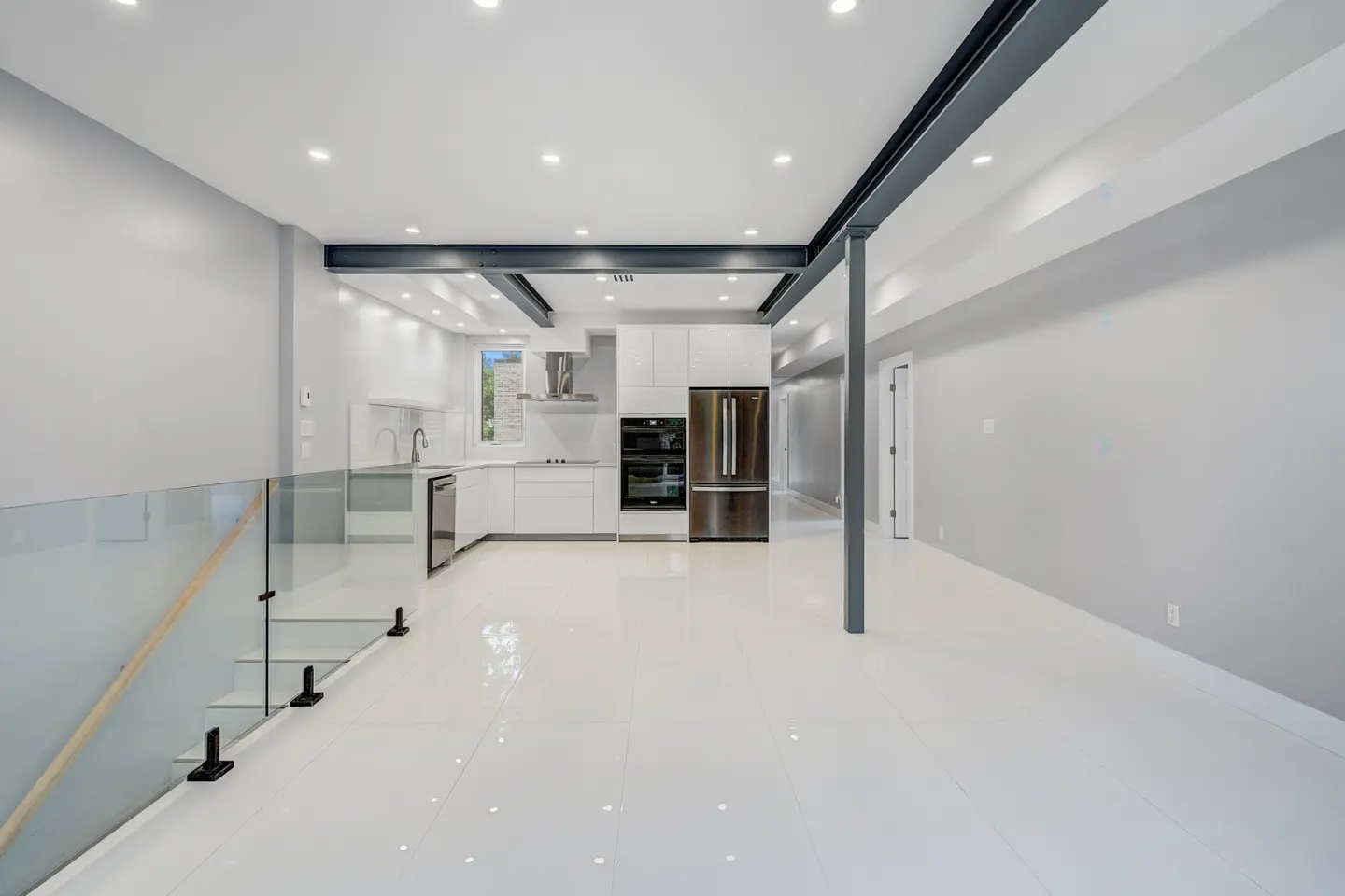 Bright, modern kitchen with white cabinets, stainless steel appliances, and white tile floors. Gray walls and steel beams add contrast.