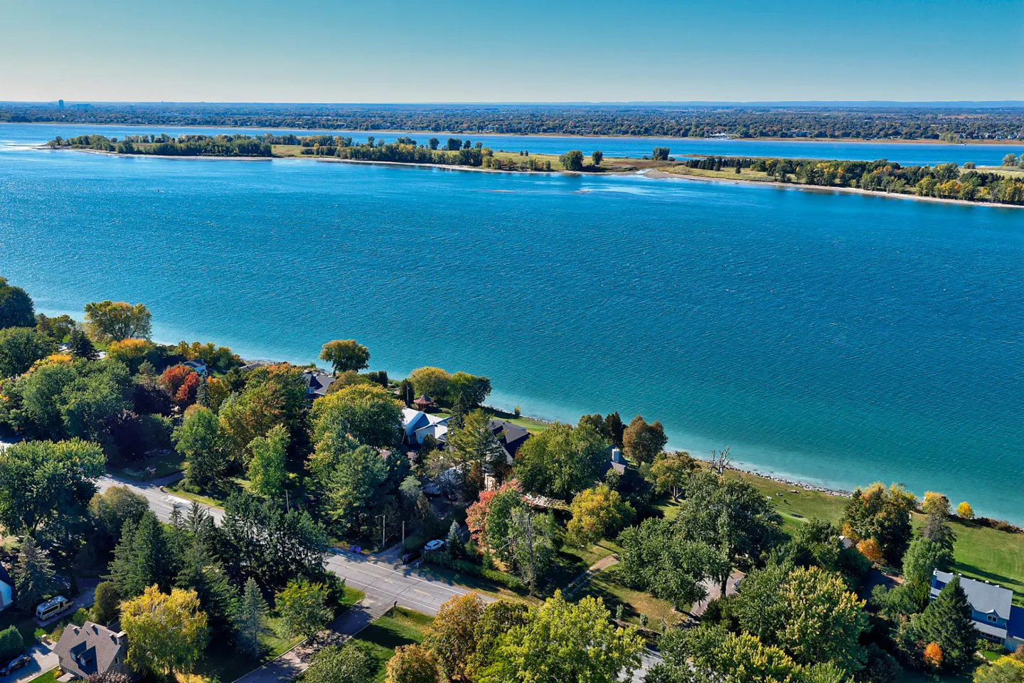Aerial view of waterfront homes nestled among trees with blue water and islands in the background.