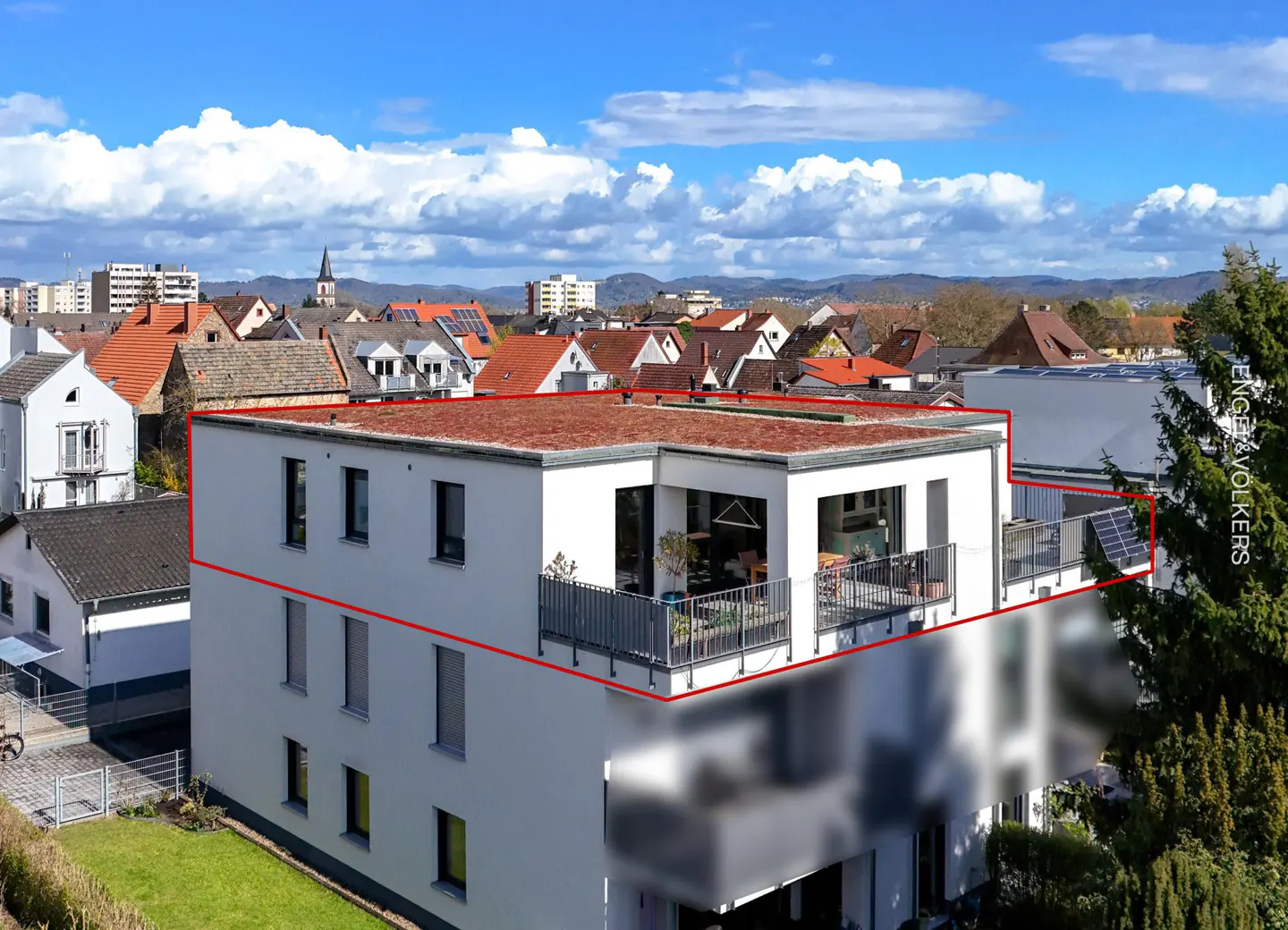 Modern white building with a flat roof and balconies, outlined in red, against a backdrop of rooftops and a blue sky with clouds.