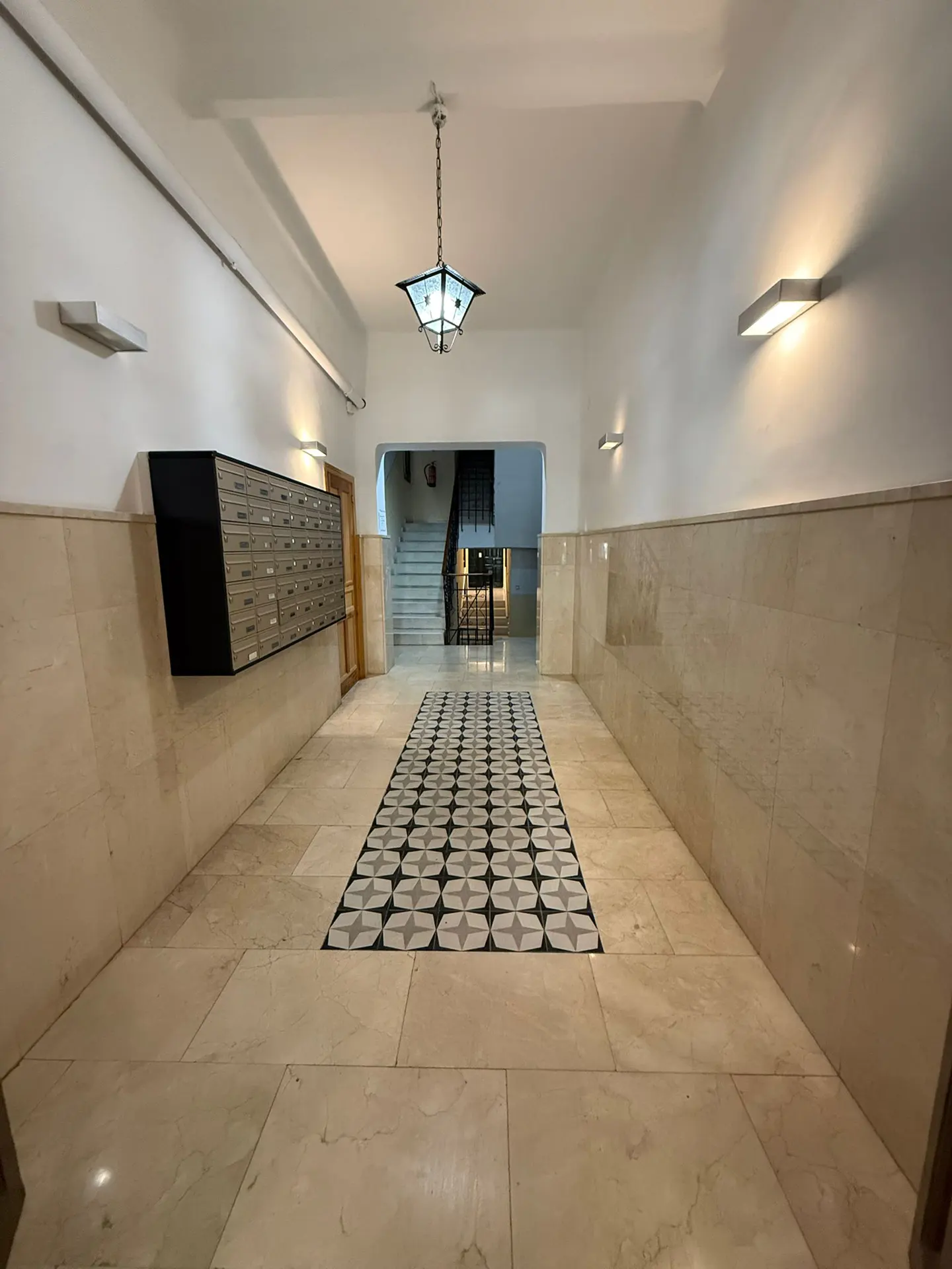Apartment building hallway with marble walls, tile floor, mailboxes, and stairs in the background.