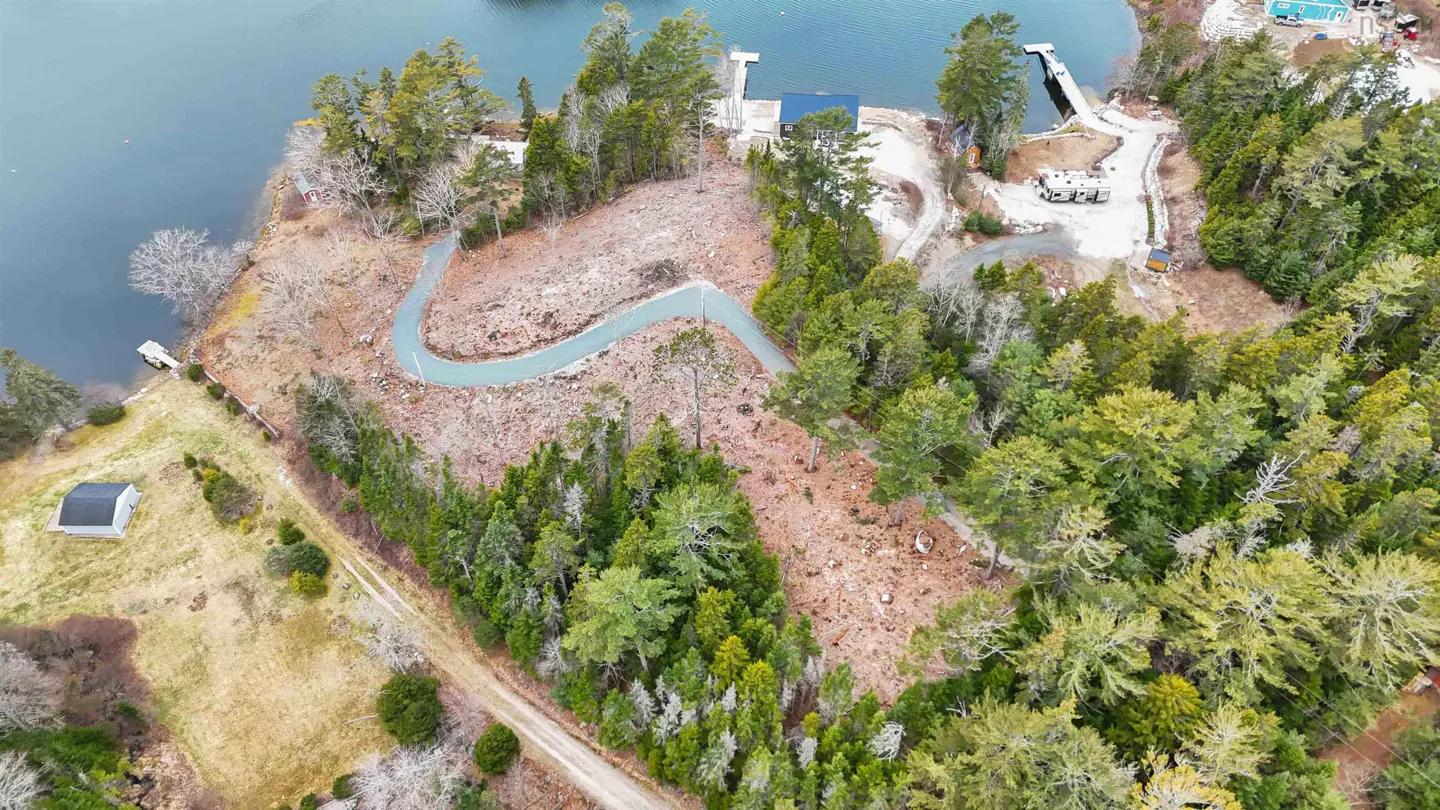 Aerial view of a waterfront property with a winding driveway, trees, and a small building near the water.