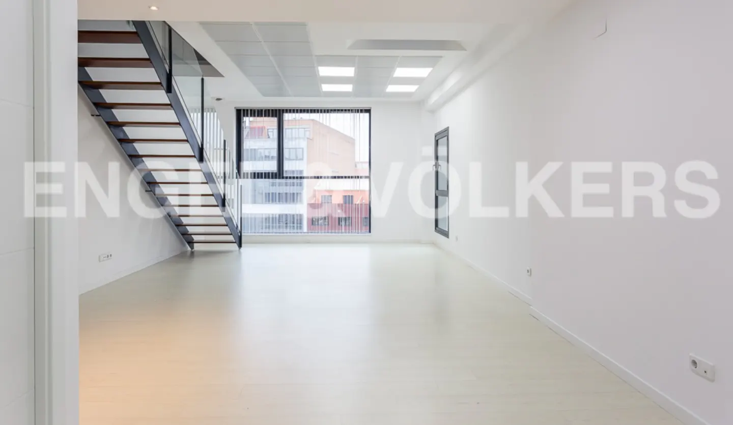 Bright, empty room with white walls, light wood floors, and a modern staircase with wood treads and metal railings. Large window with city view.