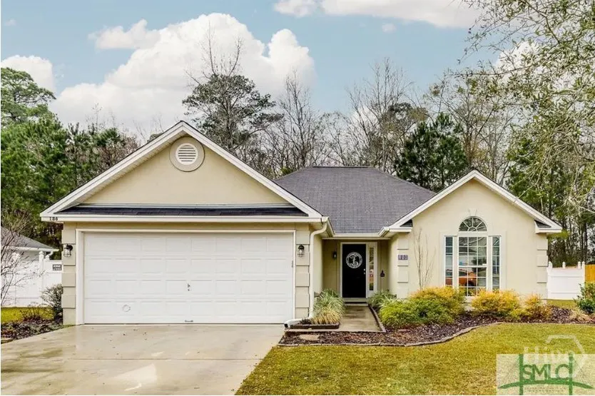 Beige single-story house with a white garage door, black roof, and a black front door with a wreath.