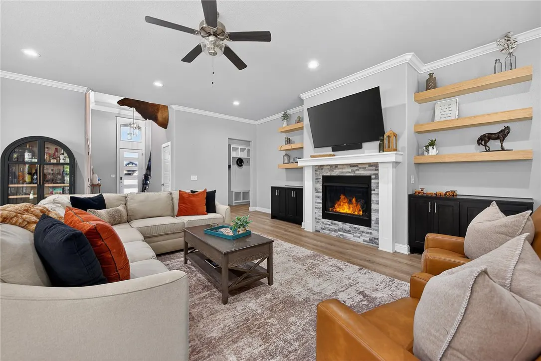 Living room with a beige sectional sofa, brown leather chairs, and a fireplace with a TV above it.