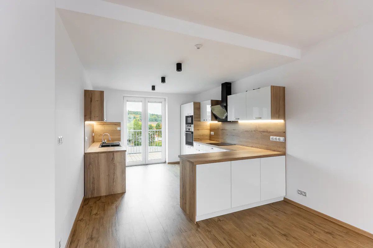 Bright, modern kitchen with white cabinets, wood countertops, and wood-look flooring. A balcony door lets in natural light.