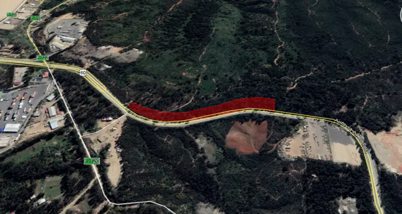 Aerial view of a highway, marked in red, running through a green, tree-covered landscape.