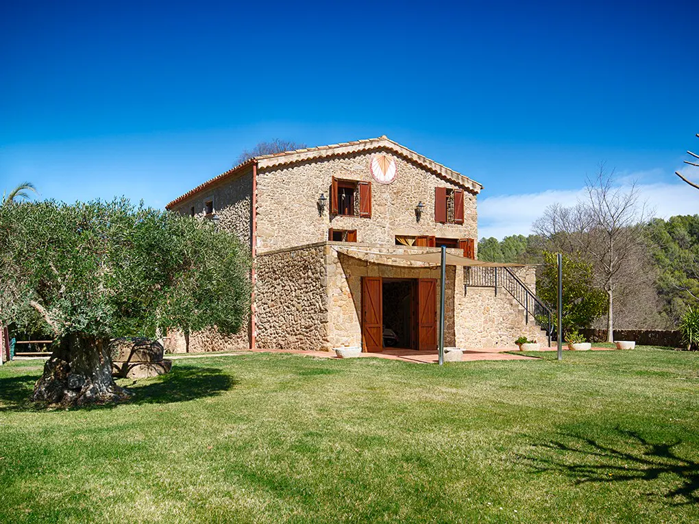 Stone house with red shutters and a sundial on a green lawn under a blue sky.