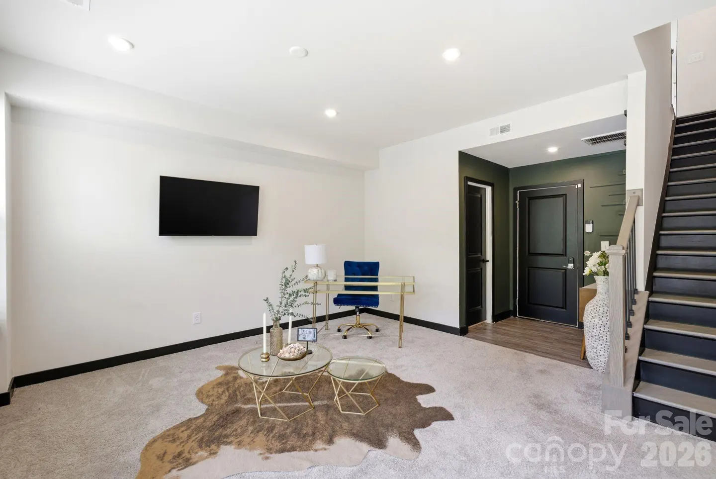 Bright room with white walls, a black TV, a gold desk and tables, a blue chair, and a staircase.