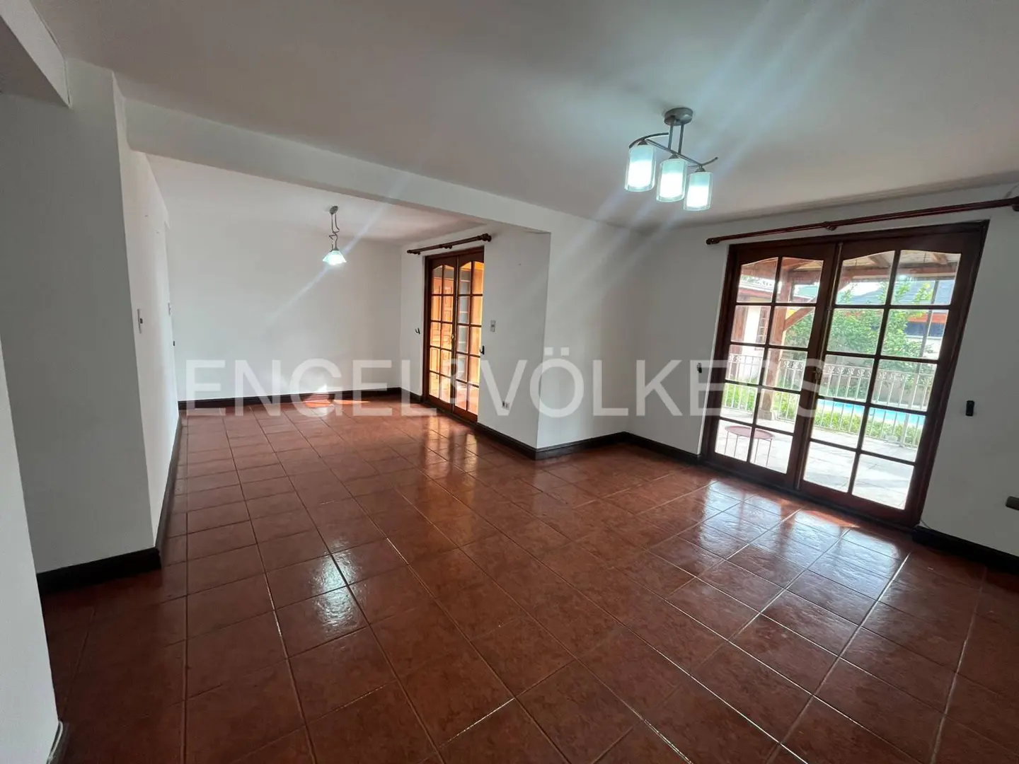 Spacious, empty room with white walls, terracotta tile floors, modern light fixtures, and glass doors leading to a patio.