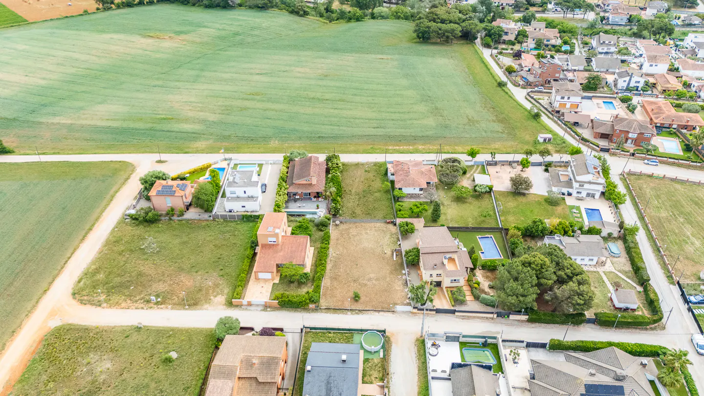 Aerial view of a residential area with houses, green fields, and roads on a sunny day.