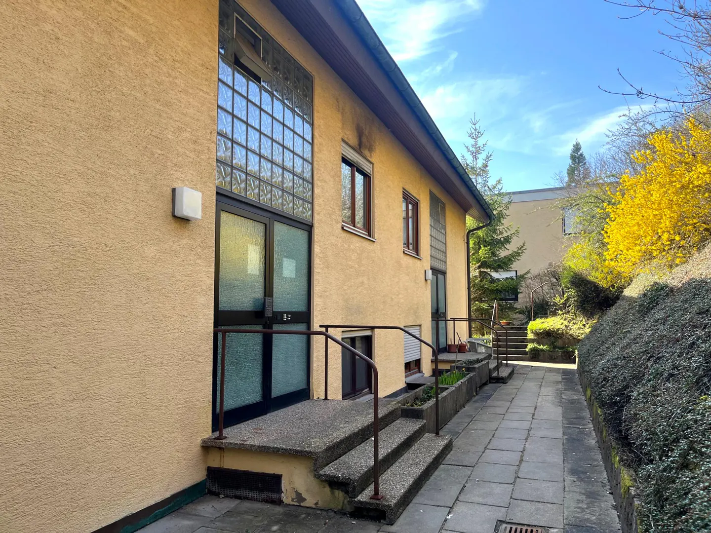 Exterior view of a yellow building with glass block windows and a stone walkway.