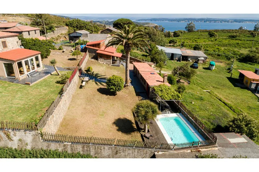 Aerial view of a rural property with stone houses, a pool, and a palm tree, near a body of water.