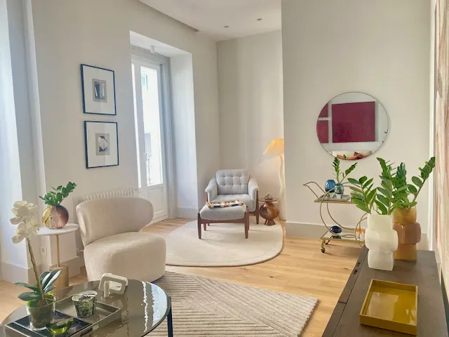 Bright living room with white walls, light wood floors, and neutral furniture. Art, plants, and a bar cart add pops of color.