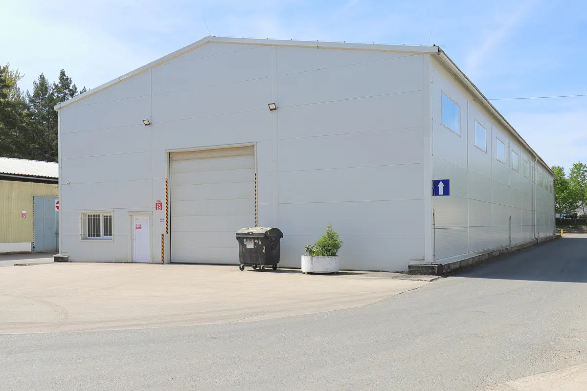 A large, white, industrial building with a roll-up door and a blue arrow sign.