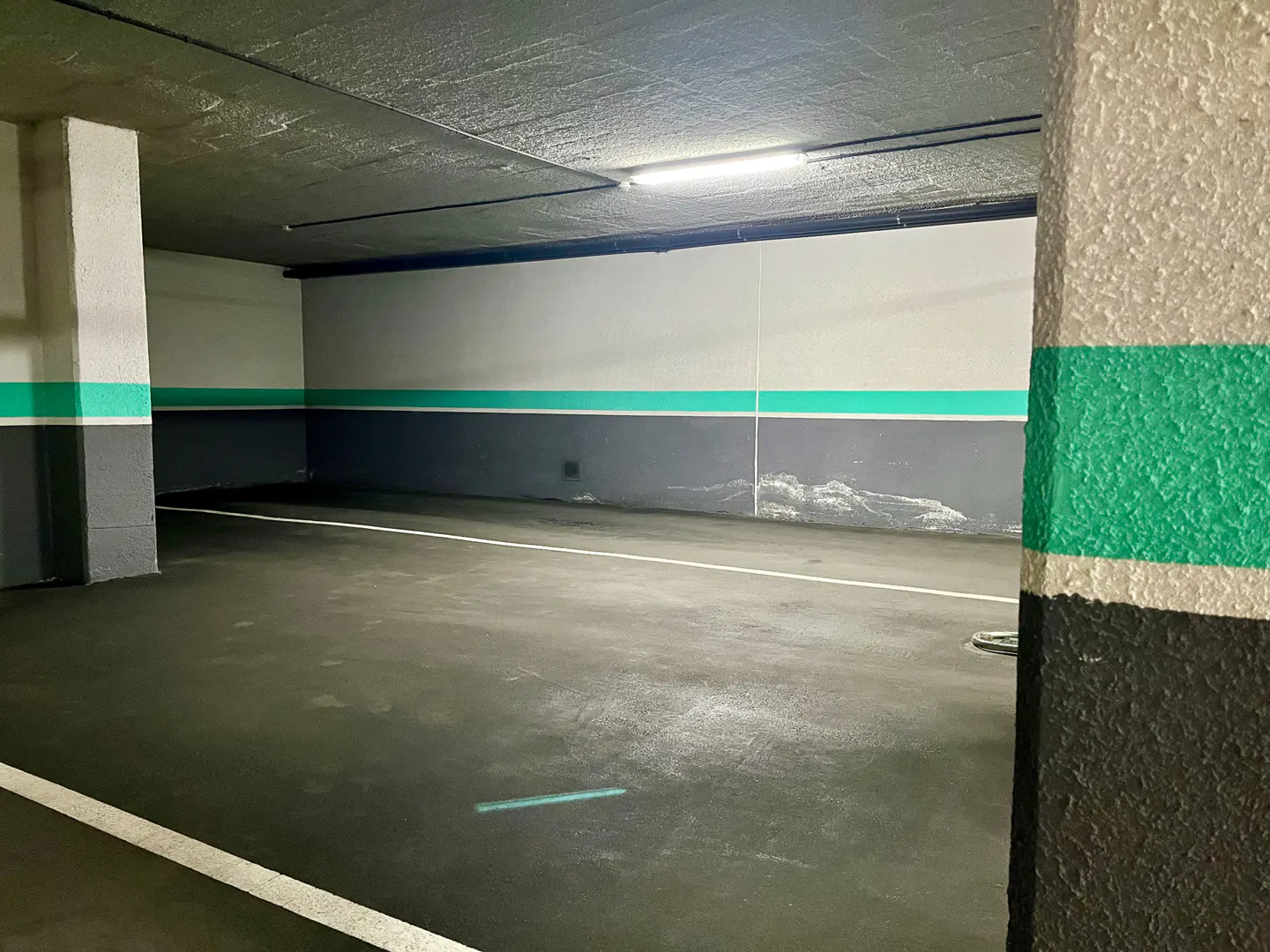 Empty parking space in a garage. Walls are painted white and gray with a green stripe. A white line marks the parking spot.