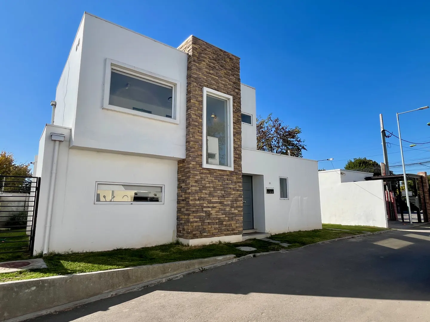 Two-story modern white house with a stone accent wall and large windows under a clear blue sky.