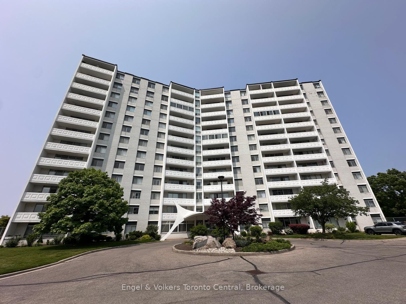 Low-angle view of a tall, light-grey residential apartment building with many balconies under a clear blue sky. [AI-generated text]