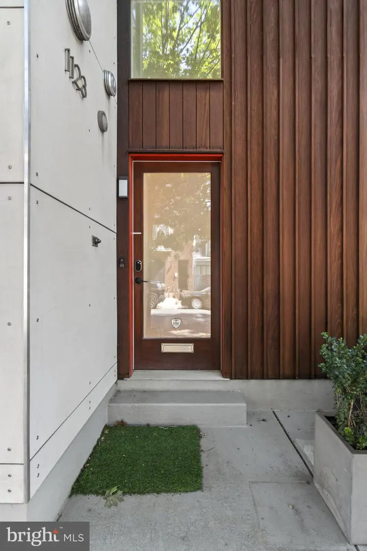 Modern home exterior with a brown wood door and paneling, white siding, and concrete steps. A small patch of green grass is near the entrance.