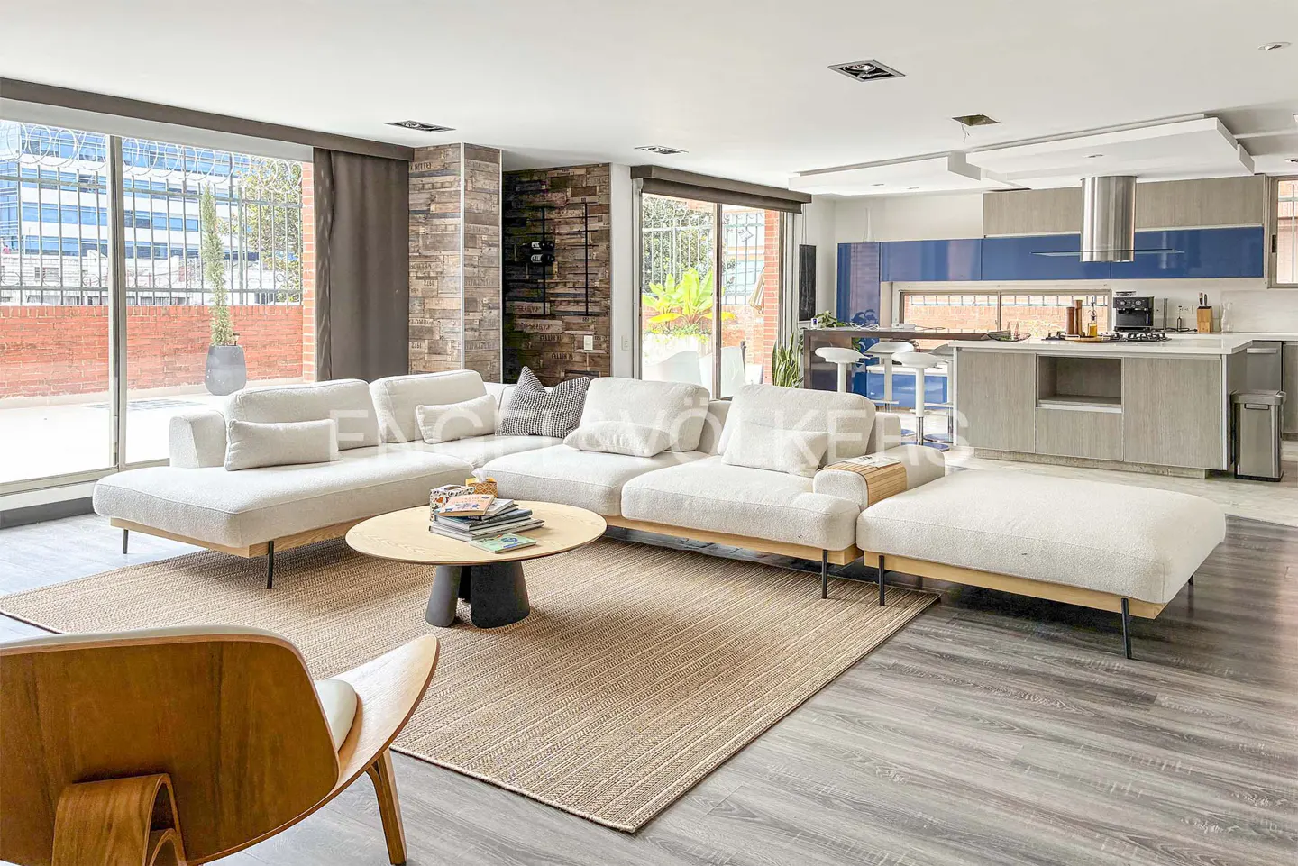 Open concept living room with a white sectional sofa, round wood table, and a tan rug. The kitchen has blue and gray cabinets.