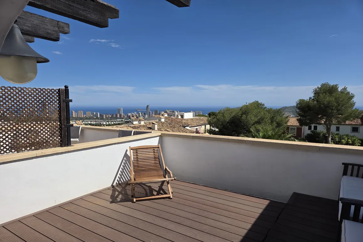 Balcony view with a wooden chair overlooking the city and ocean under a clear blue sky.
