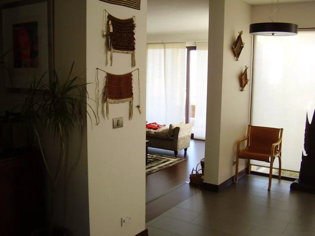 Interior view of a living room with a brown chair, a sofa, and decorative wall hangings. The room is bright with natural light.