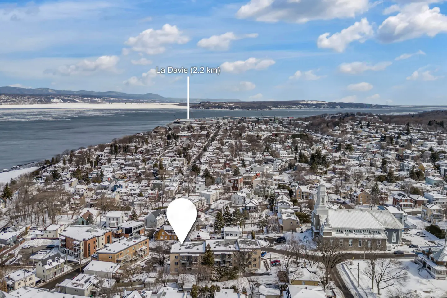 Aerial view of a snow-covered town with a white map pin over a building, and "La Davie (2.2 km)" labeled in the background.