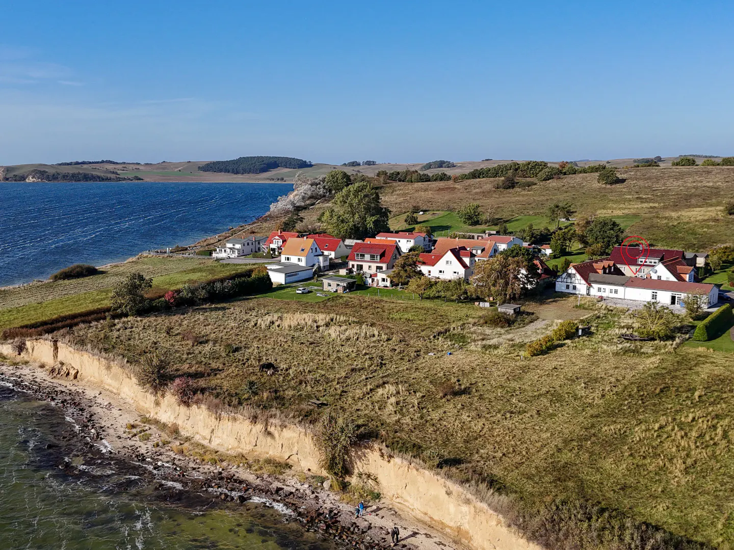 Coastal village with red-roofed houses on a grassy cliff overlooking a blue sea under a clear sky.