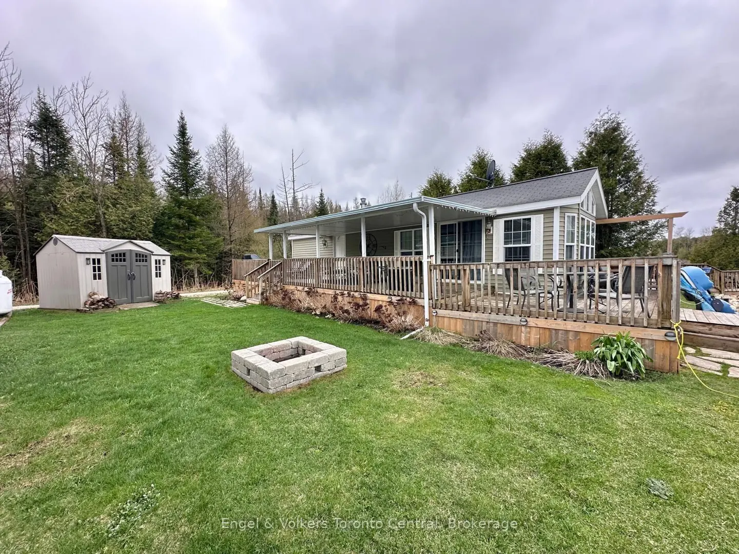 Exterior view of a green house with a wooden deck, a shed, and a fire pit on a green lawn.