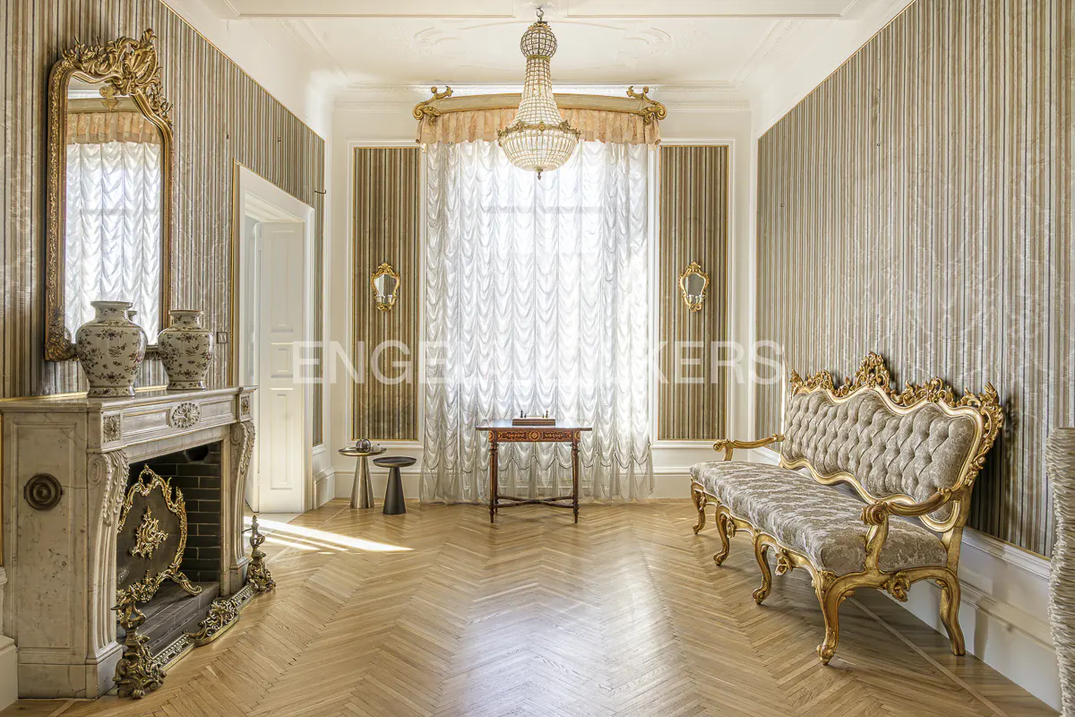 Ornate living room with herringbone wood floors, fireplace, gold sofa, and chandelier.