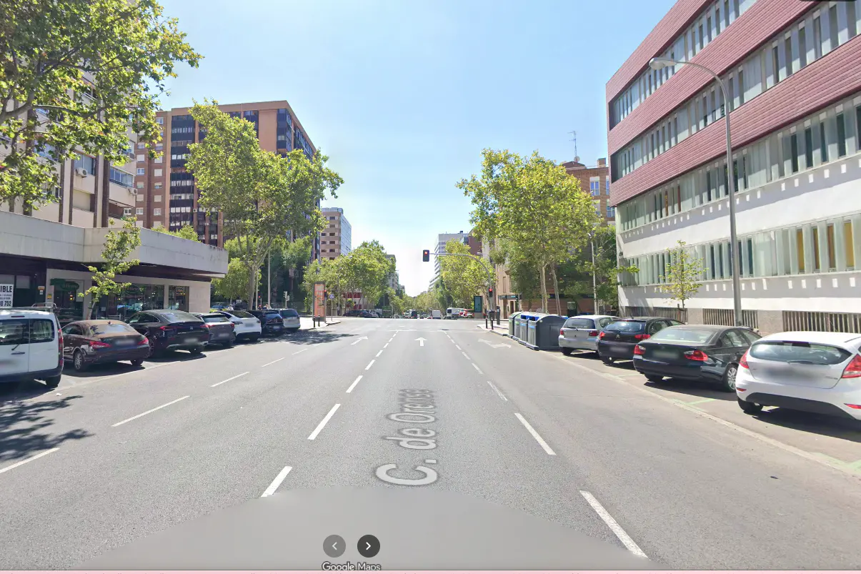 Street view of C. de Orense, Madrid, with parked cars lining both sides of the road and buildings in the background.